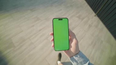 Yeşil ekran yürüyüşlü, el ele tutuşan ve dikey olarak telefonu kaydıran adam. Gün ışığında arka planda. Akıllı telefondan yazıyorum.