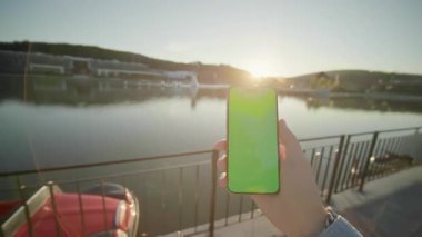 Yeşil ekran hareket ederken el ele tutuşup dikey telefon çekimleri. Arka plandaki gölde, güneş ışığında. Doğa