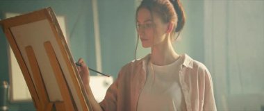 Çekici genç kadın ressamı, ışık sanatları stüdyosunda tuvale fırça ve palete resim çiziyor. Çalışma alanı. Yaratıcı