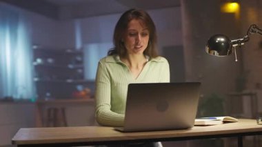 Akşamları klavyede yazı yazan düşünceli beyaz kadın. Modern oturma odasındaki masada oturan çekici bir kızın görüntüsü. Akşam vakti. Lambalar. 360 derecelik izleme atışı