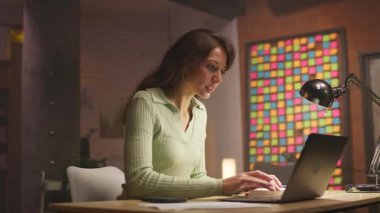 Odaklanmış kadın uzaktan çalışan dizüstü bilgisayarda oturuyor ve masada oturuyor. Düşünceli genç beyaz kadın makale okuyor ve klavyede daktilo yazıyor. İçeride. Daire. 360 derece izleme