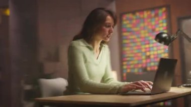 Oturma odasında dizüstü bilgisayar kullanan kendinden emin, mutlu, üretken, beyaz bir kadın. Geceleri oturma odasında çalışan güzel bir kızın görüntüsü. Hız kavramı. Kamera hareket ediyor