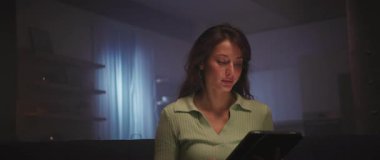 Akşamları oturma odasında kanepede otururken siyah tablet kullanan güzel bir esmer görüntüsü. Odaklanmış genç bir kadının ekrandaki cihaza dokunuşunun görüntüleri. İz sürme sahnesinde hareket