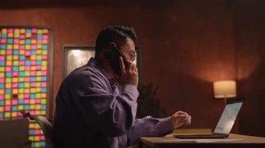 Gözlüklü Asyalı iş adamını dizüstü bilgisayar kullanarak ve defterini açarak kapat. Telefonda konuş. Geceleri ekrana ciddi ciddi bak. 360 derece. Etrafta dolanıyorum.