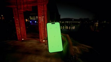 Açık havada dikey pozisyonda yeşil ekranlı cep telefonu kullanan erkekler. Akşamları merdivenlerde otururken elinde akıllı telefon tutan adam. Tatil köyü. Model, kroma anahtarı