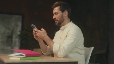 Masada oturan yakışıklı başarılı sakallı adam ekranda gülümseyen ve tatmin olan telefon görüntüsü kullanıyor. Modern ofis. 360 Derece