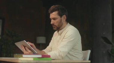 Masada oturan yaratıcı sakallı adam, ofiste çalışan tablet bilgisayardaki kalem boyasını tutuyor. Düşünüyorum. Kamera hareket ediyor. 360 Derece