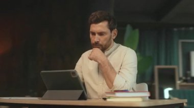 Masada oturan ciddi bir adamın portresi ofiste tablet bilgisayar kullanıyor. Düşünüyorum. Kamera hareket ediyor. 360 Derece