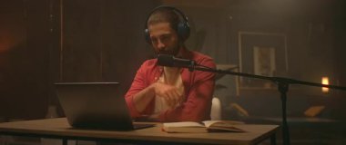 Genç ve mutlu radyo sunucusu dizüstü bilgisayarla masada oturuyor ve ekrana bakıyor. Yayıncılık sırasında eğlenen rahat bir adam. Radyo yayını. Genç ve çekici bir adam şarkı söylüyor.