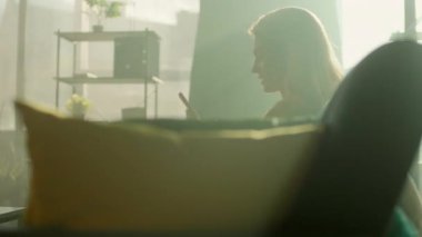 Çekici genç bir kadın evinde koltukta oturup telefonla mutlu ve gülümsüyor. Odada güneş ışığı var. Kamera hareket ediyor. 360 derece