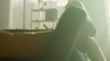 Üzgün kadın evde, koltukta oturup telefonla düşünüyor. Odada güneş ışığı var. Kamera hareket ediyor. 360 derece