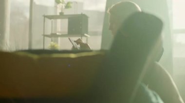 Tablet bilgisayar kullanarak koltukta oturan gülümseyen kadın kendini mutlu hissediyor. Odada güneş ışığı var. Dinlenme zamanı. Kamera hareket ediyor. 360 derece