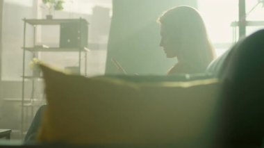 Acaba evdeki kanepede oturan mutlu genç bir kadın telefonla gülümsüyor mudur? Odada güneş ışığı var. Kamera hareket ediyor. 360 derece