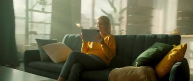 Evdeki kanepede oturan kadının yanında hareket eden bir kamera tablet bilgisayar kullanarak mutlu bir şekilde gülümsüyor. Odada güneş ışığı var. Dinlenme zamanı. Haberler iyi. 360 derece