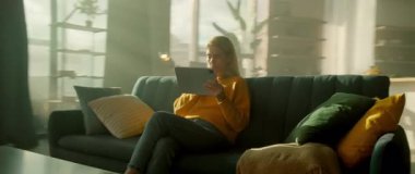 Evdeki kanepede tablet bilgisayar kullanan ciddi bir kadın. Odada güneş ışığı var. Dinlenme zamanı. Kamera hareket ediyor. 360 derece