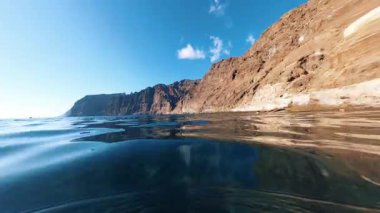 Güneşli havalarda kıyı manzarası muhteşemdir. Güzel mavi gökyüzü, vahşi kayalar ve suda yüzen insanlar. Su yüzeyinde FPV.