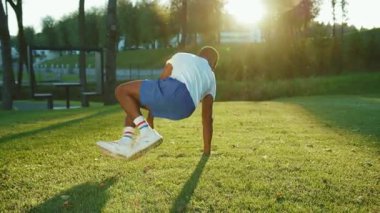 Afrika kökenli Amerikalı sporcu break dans yapıyor. Arka planda çimlerin üzerinde harika dublörlük yapıyor. Yetenekli sporcu antrenmandan önce ısınıyor..