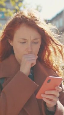 Bu videoda, kızıl saçlı bir kadın telefonuyla iletişim kuruyor, bağlantı ve merakını gösteriyor, kahverengi ceketli bir kadın da aynı şeyi yapıyor.