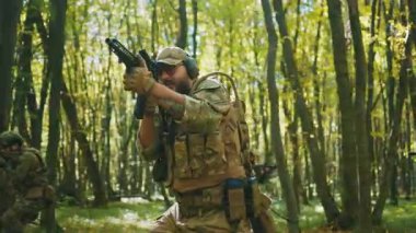 Kamuflaj üniformalı ve silahlı bir grup asker güneş ışığı ormanında yavaşça yürüyor. Miğferdeki askeri keskin nişancı. - Savaş. Koruma