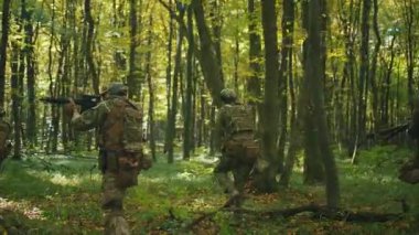 Orman askerleri kamuflaj üniformalarıyla ve silahlı bir şekilde gün ışığına bakarak yavaşça yürüyorlar. Miğferli askerler. - Savaş. Koruma
