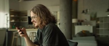 Şık gözlükler takan genç bir adam, şık ve modern bir çalışma ortamı içinde akıllı telefonunu kullanıyor.