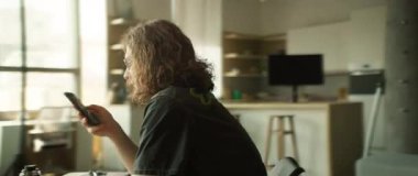 Şık gözlükler takan genç bir adam, şık ve modern bir çalışma ortamı içinde akıllı telefonunu kullanıyor.