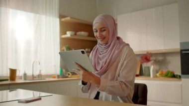 Mutfakta Müslüman bir kadın evdeki sandalyede oturan tablet bilgisayar kullanıyor. Kamera hareket ediyor. 360 derece