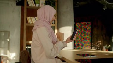 Tesettürlü Müslüman kadın, video konuşmasında duygusal bir şekilde evdeki gün ışığında konuşuyor. Gülümseyerek mutlu ol. Kamera hareket ediyor. 360 derece