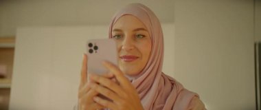 Başörtülü Müslüman kadın, evde gün ışığında sosyal medyayı kullanıyor. Gülümseyerek mutlu ol. Kamera hareket ediyor. 360 derece
