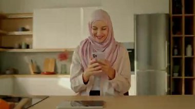 Müslüman kadının tesettürlü videosu evde otururken cep telefonuna mesaj yazıp mutlu mesut gülümsemesini sağlıyor. Kamera hareket ediyor. 360 derece
