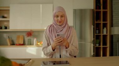 tesettürlü müslüman kadına bak. Gün ışığında evde oturup mesaj yazan telefon kullan. Gülümseyerek mutlu ol. Kamera hareket ediyor. 360 derece