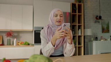 Mutlu tesettürlü Müslüman kadın evde otururken telefon mesajı yazıyor. Kamera hareket ediyor. 360 derece