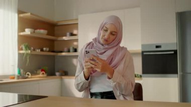 Mutlu Müslüman kadın tesettüre telefon açıp evde oturup dans ediyor ve gülümsüyor. Kamera hareket ediyor. 360 derece