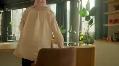 Zaman aşımı videosu. Türbanlı Müslüman kadın modern güneş ışığı mutfağında meyve suyu içiyor. Kamera hareket ediyor. 360 derece