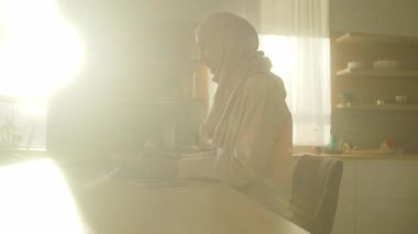 Evde masadaki dizüstü bilgisayarda çalışan, tesettürlü Müslüman iş kadınına bakın. Güneş ışığı. Kamera hareket ediyor. 360 derece