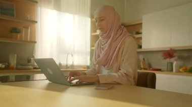 Evde masadaki dizüstü bilgisayarda çalışan, tesettürlü Müslüman iş kadınına bakın. Güneş ışığı. Kamera hareket ediyor. 360 derece. Zaman aşımı