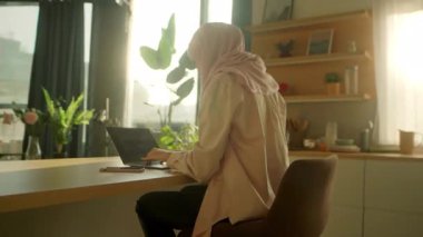 Evde masa başında çalışan tesettürlü Müslüman bir iş kadını. Yorgun hissediyorum. Güneş ışığı. Kamera hareket ediyor. 360 derece