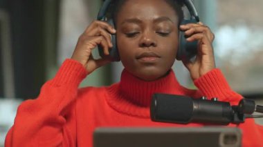 Kadın podcaster 'ın kulaklık takıp müzik dinlerken çekilmiş yatay görüntüleri. 360 derecelik izleme atışı. Kamera hareket ediyor. Sinema etkisi. Stüdyo konseptiyle yayın yapmak. Kapalı