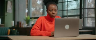 Parralax etkisi. Masada otururken gümüş dizüstü bilgisayar kullanan yakışıklı Afro-Amerikan bir kadının 360 derecelik görüntüsü. Odaklanmış turuncu kazaklı kız internette geziniyor. İz sürme