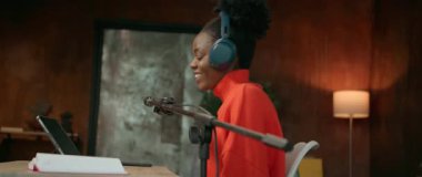 İş yerinde oturan, kulaklıklı, gülümseyen, Afro-Amerikan güzel bir kadının yatay görüntüleri. Çalışırken mikrofon kullanan kadın radyo sunucusu. Dijital tablet kullanan bir kız. Parallaks