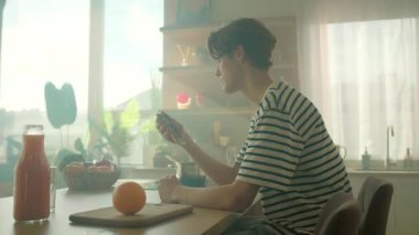 Genç beyaz bir adam mutfakta akıllı telefon kullanıyor. Sosyal medyada fotoğraf izlerken internette vakit geçiren mutlu bir adam. Mobil teknoloji konsepti. İnternet bağımlılığı. Parallaks etkisi. Kamera.