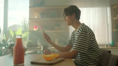 Sarı akıllı telefonu elinde tutan neşeli, genç, beyaz bir adam ekrandaki alete bakıyor. Mutfakta mesaj okuyan mutlu adam. İz sürme hareket ediyor. İçeride. Parallaks etkisi