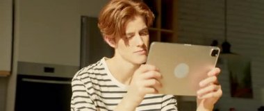 Kafkasyalı genç bir adamın yemek masasında oturup dijital tablet ekranına baktığı görüntüler. 360 derecelik izleme atışı. Cihazla ilgili e-kitap okuyan düşünceli bir adam. Parallaks etkisi. Mutfak.