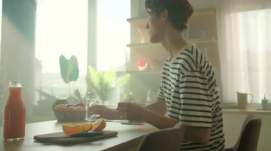 Yakışıklı beyaz bir adam bardağa portakal suyu döküyor. Mutfaktaki kahvaltı masasında oturan adamın görüntüsü. Sağlıklı yaşam tarzı kavramı. İçeride. Dönme açısı. Parallaks etkisi. Günaydın.