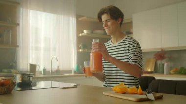 Kahvaltıda gülümseyen bir gencin portakal suyu döktüğü 360 derecelik bir çekim. Modern mutfaktaki yakışıklı beyaz adamın elinde cam tutarken ki görüntüsü. Gündüz vakti. Kamera hareket ediyor