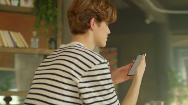 Yakın plan gülme görüntüsü, akıllı telefon ekranına bakan günlük kıyafetler içindeki beyaz bir adamı şaşırttı. Modern mutfaktan duygusal yakışıklı bir adam arıyor. Konuşma konsepti