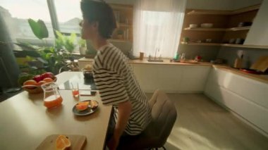 Mutfak 360 derece. Genç bir adamın rahat sandalyeye oturup elinde turuncuyla akıllı telefondan sohbet ederken görüntüsü. Sosyal medya yayınına kayan adam. Samimi stüdyo. Ev