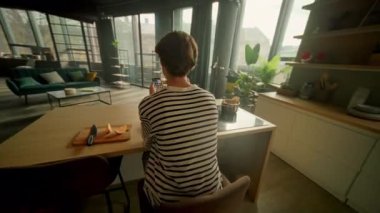 Modern stüdyonun mutfağında akıllı telefondan sohbet ederken odaklanmış yakışıklı, beyaz bir adamın portakal suyu içerken 360 derecelik görüntüsü. Kahvaltı masasında oturan mutlu adam. Sinematik