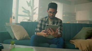 Kameralar gözlüklü genç adamın yanında hareket ediyor. Evdeki kanepede oturan tablet bilgisayar kullanıyor. Düşünüyorum. İletişim. 360 derece