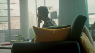 Kanepede dinlenen gözlüklü yakışıklı genç adam akıllı telefon kullan. Sosyal medyada sohbet etmek. - Evde. Kamera hareket ediyor. 360 derece